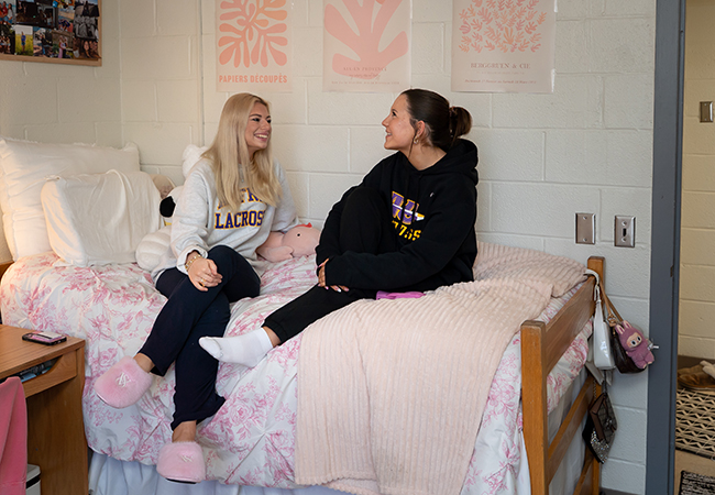 A photo of two Alfred University students sitting on a bed in a dorm room