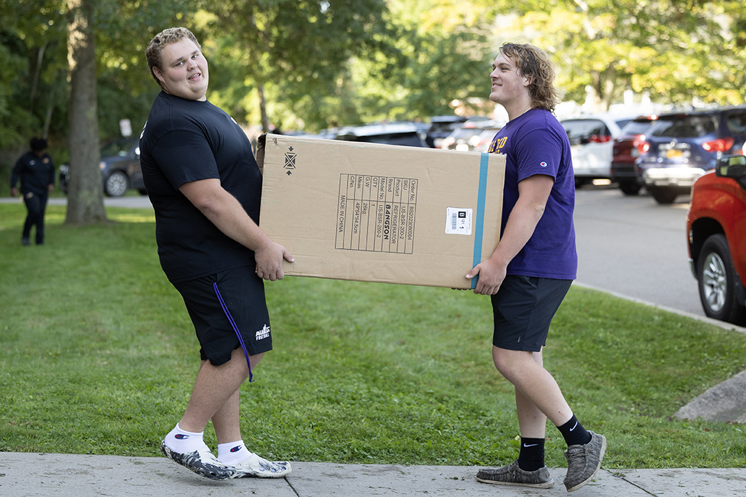 A photo of two Alfred University students carrying a large cardboard box