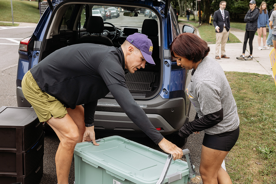 A photo of an Alfred University parent and student unloading a storage bin from the trunk of a car