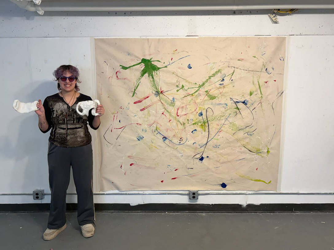 A photo of Han Ramirez-Garcia standing next to their artwork