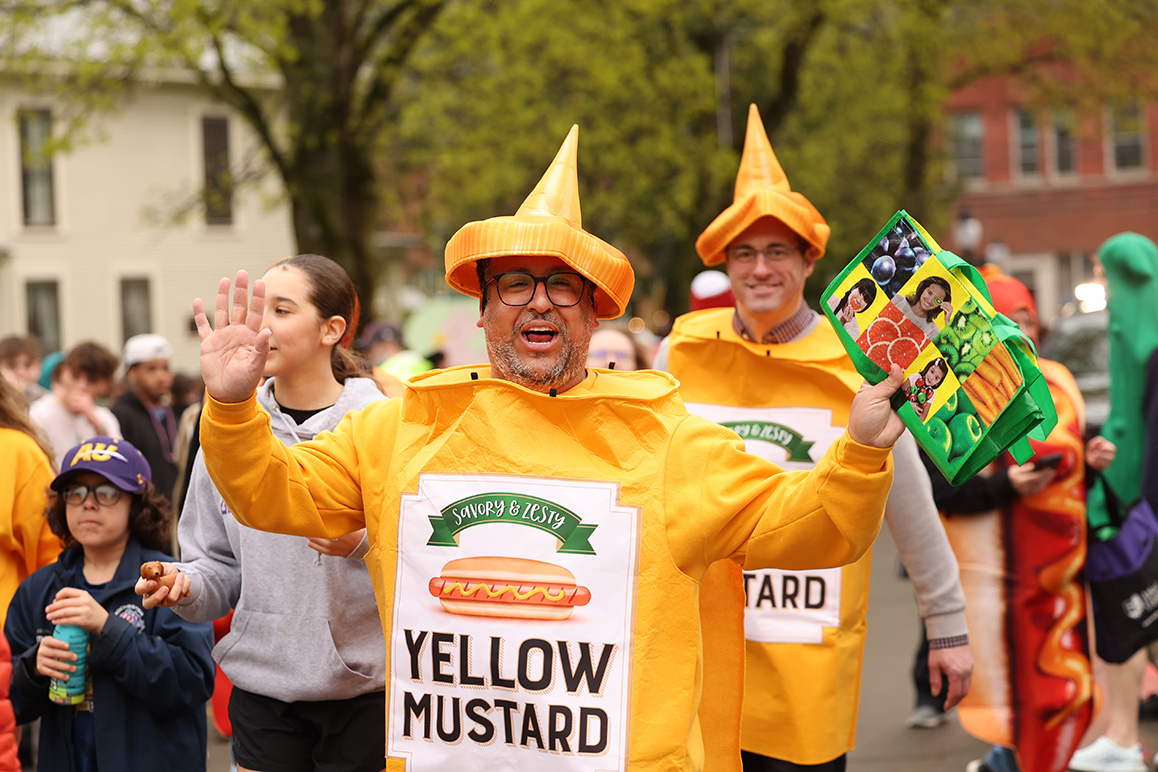 A photo of a man in a mustard costume walking down Main Street in Alfred