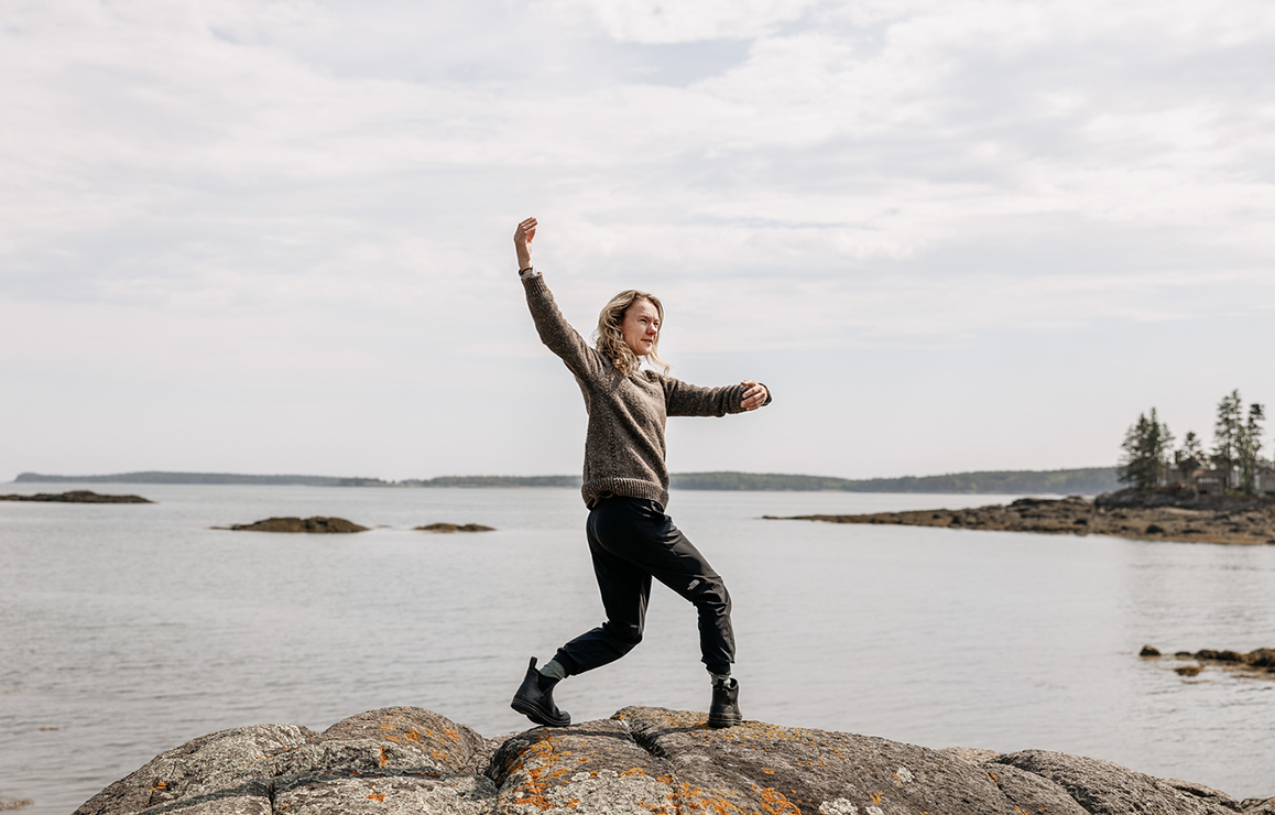 A photo of a woman dancing on a rocky coastline in Maine