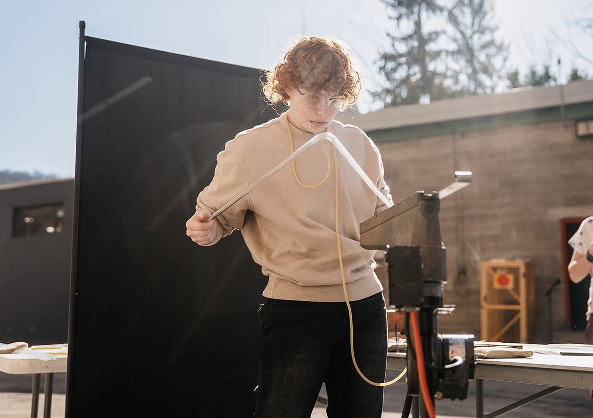 A photo of an Alfred University student bends a neon tube