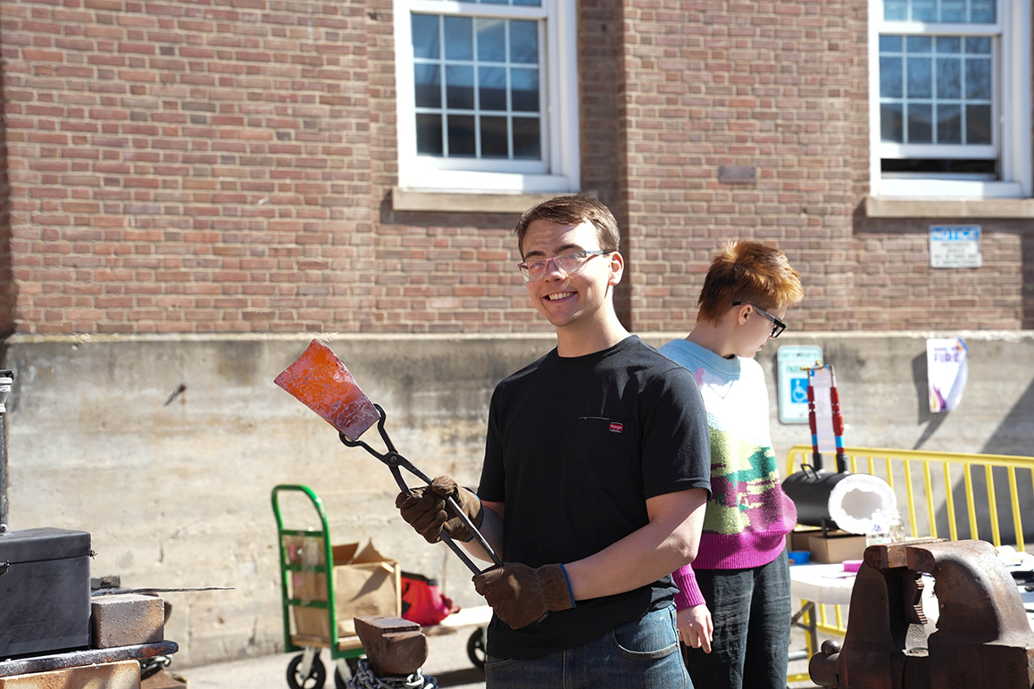 A photo of an Alfred University student holding a hot stone with tongs