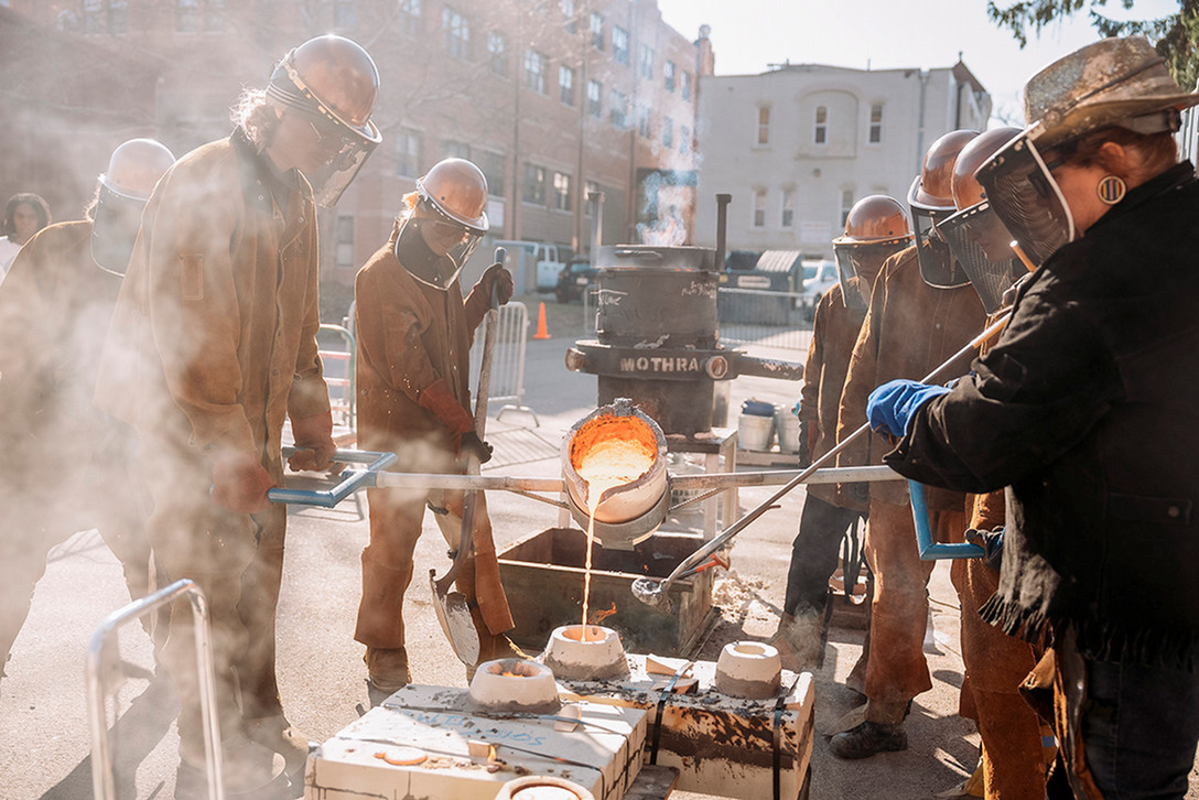 A photo of students pouring molten metal into a stone mold