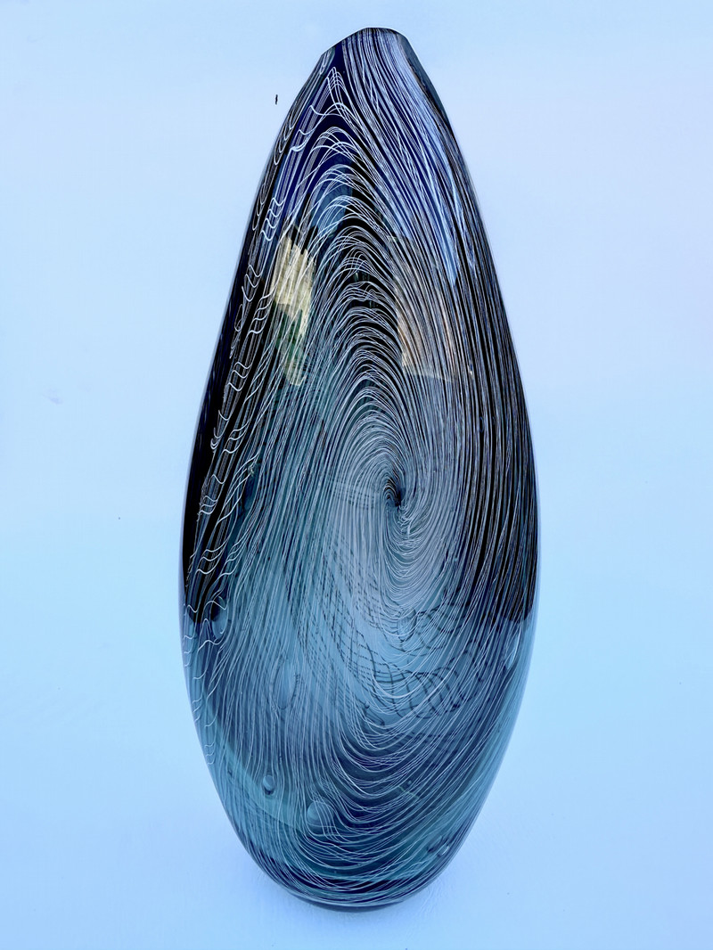 an oval glass piece that is dark blue and blue with white spirals in the middle