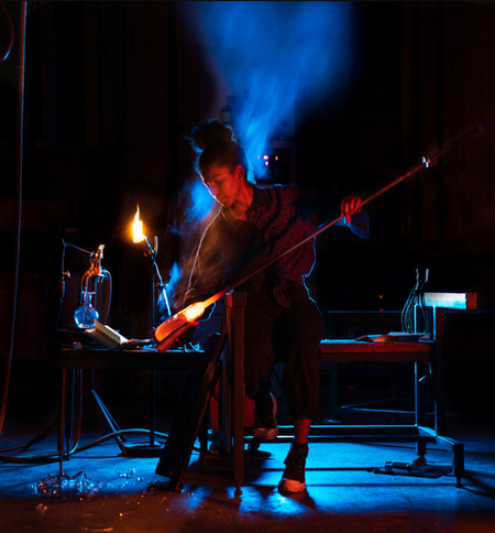 artist blowing glass in dramatic lighting black background with blue steam and vibrant fire