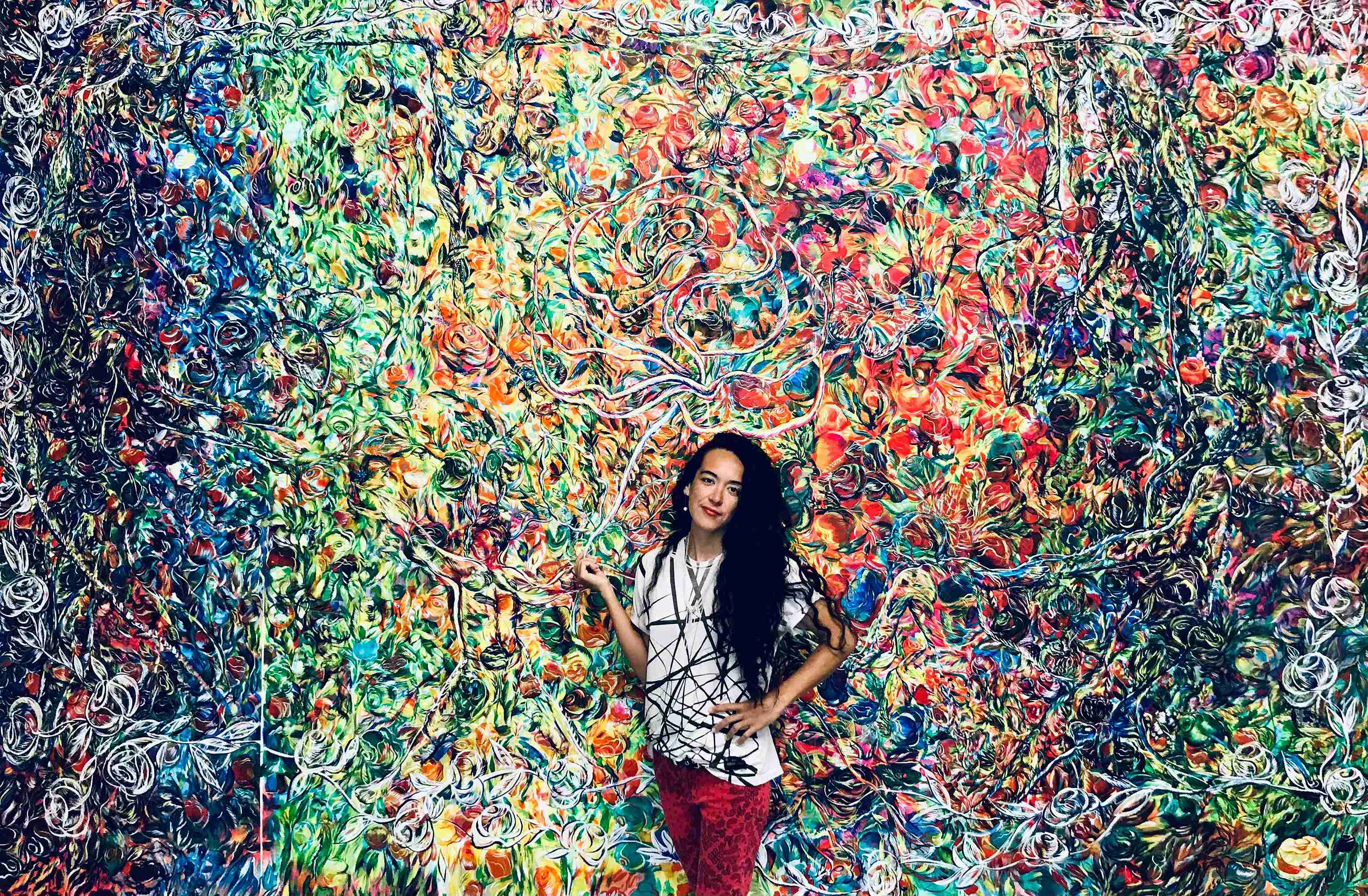 photo of the artist behind her artwork of colorful florals