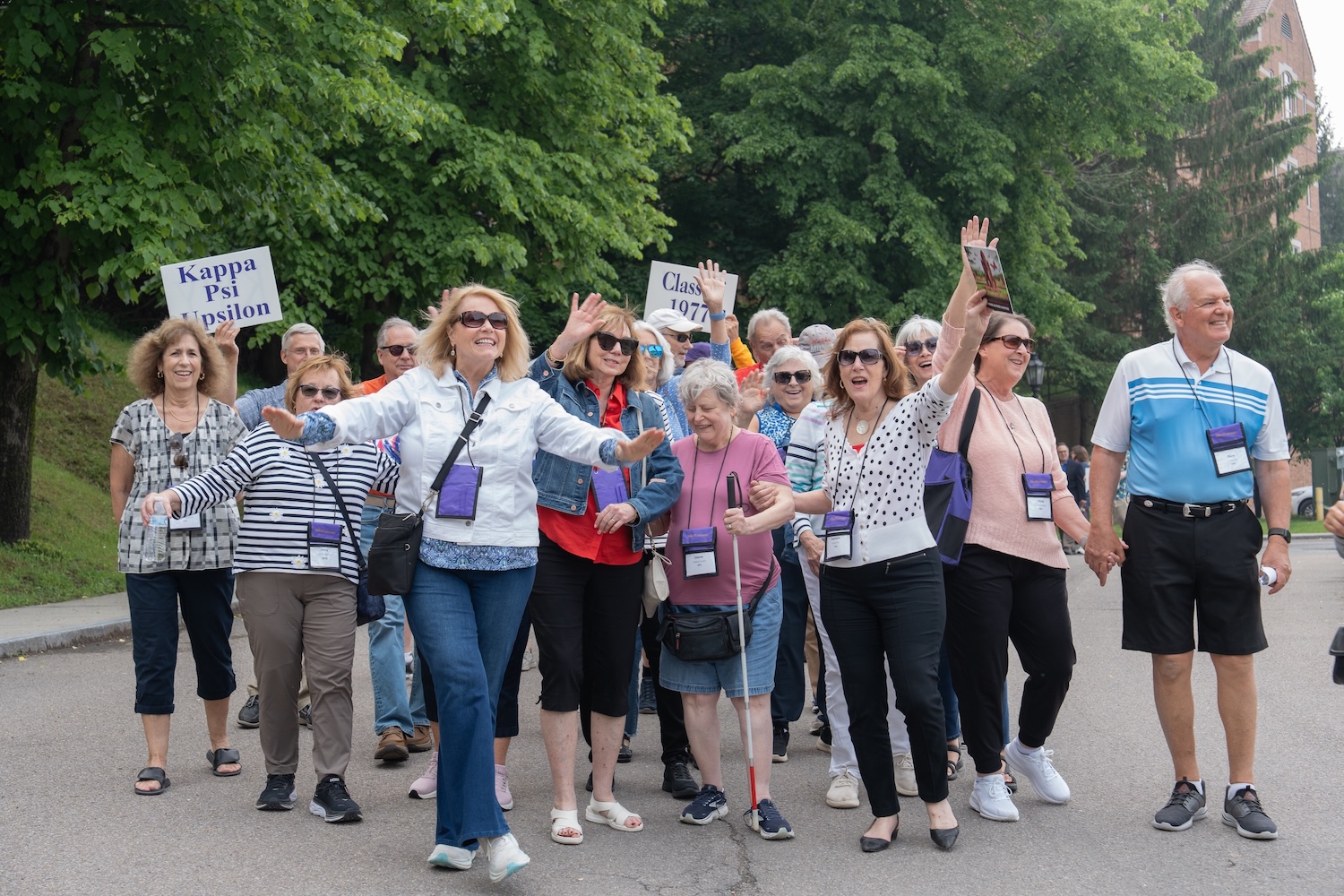 Alfred University alumni wearing name badges march together during Reunion Weekend, carrying signs for Kappa Psi Upsilon and the Class of 1977.