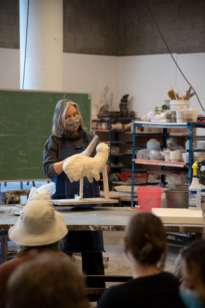 person demonstrating ceramic techniques to a group of people in studio space