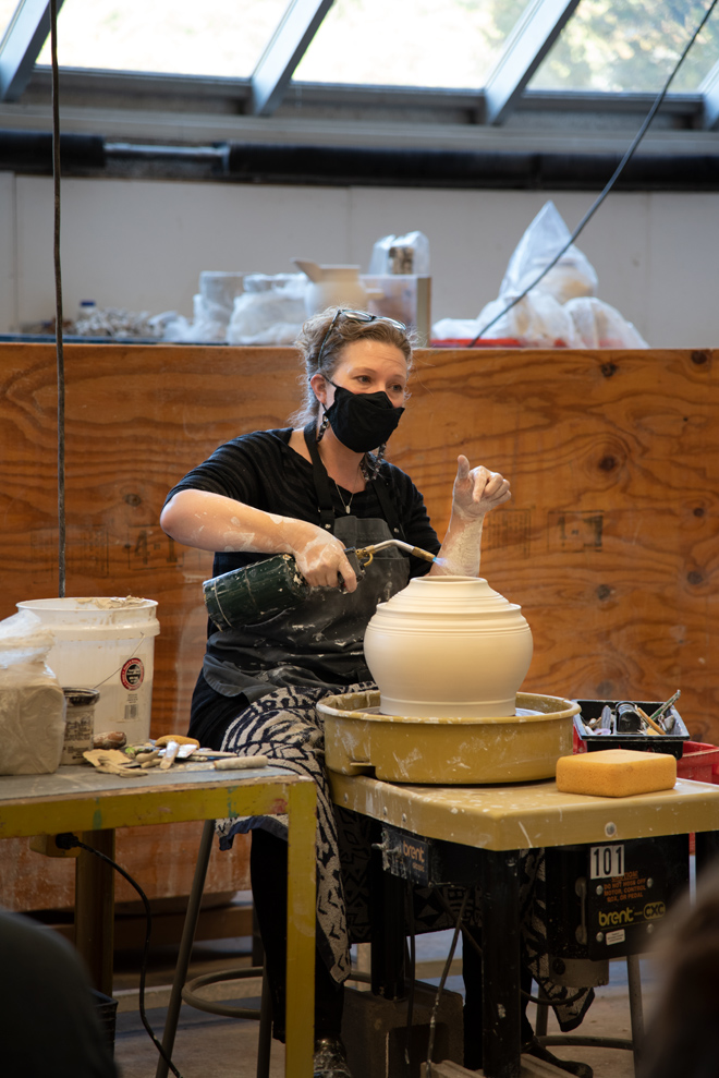 person talking to a group of people with a blow-torch  on the ceramic vase