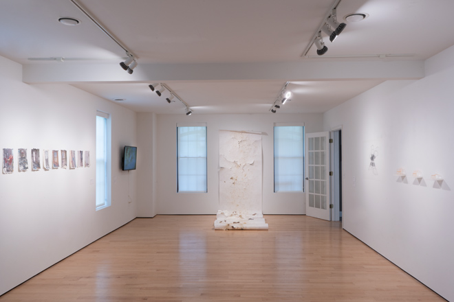 empty gallery space with artwork mounted on the walls and a large scroll material hung on the wall that also drapes onto the floor
