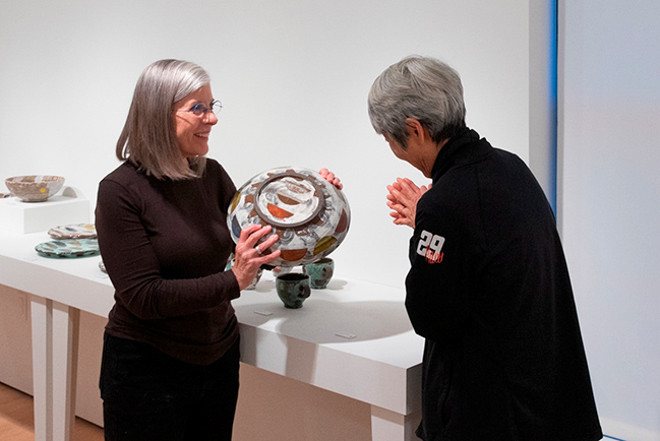 gallery staff showing off a piece of pottery to a viewer