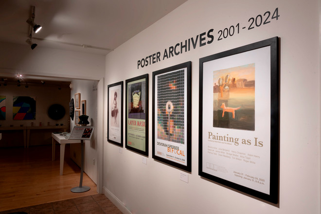 A view of the front wall of the Cohen Gallery displaying four framed posters beneath the text “Poster Archives 2001–2024.” Posters include “Painting as Is,” “Devorah Sperber: Bifocal,” “Layer Mask,” and one featuring a portrait. A hallway and additional exhibition space are visible in the background.