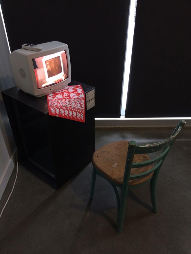 A Small TV With Red Poster on the Table and a Chair