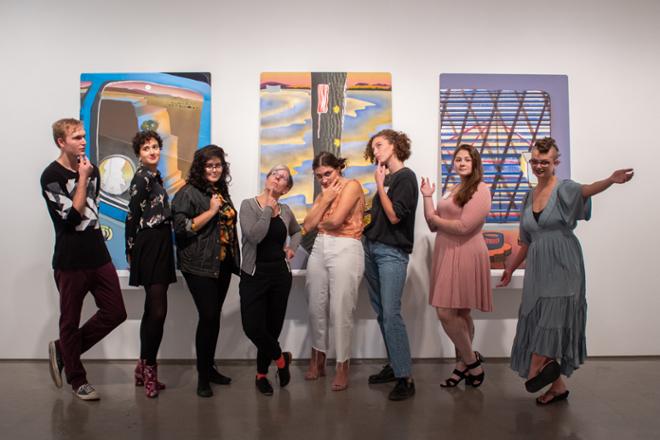 gallery staff posing jokingly together in front of exhibit artwork
