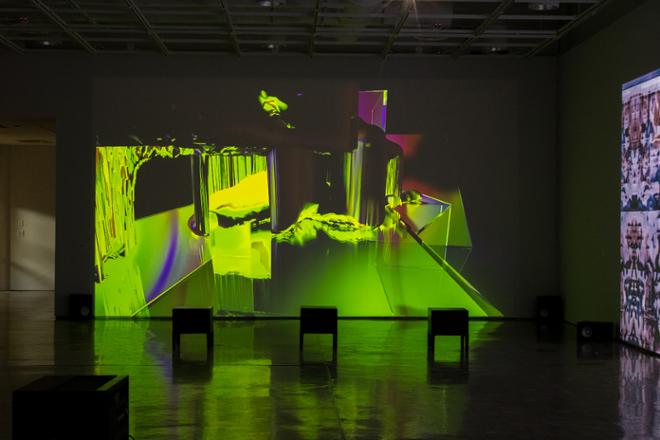 video projection still on the wall with vibrant use of green and three seats for viewing