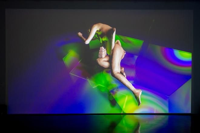 video projection still of distorted human figure lying down on vibrant multi-colored swirls as a background