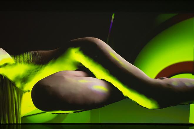 video projection still human figure lying down with bright neon yellow and green lighting