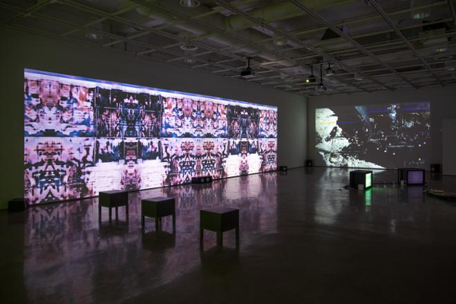 gallery space with multiple video projections on the walls and seats for viewing on the gallery floor