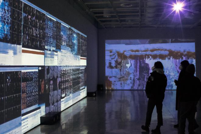 people standing in front of video projection on the gallery walls