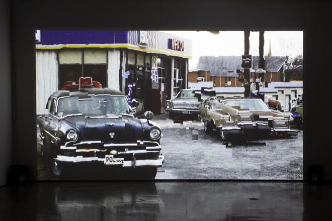 video projection still featuring old vintage beat up cars