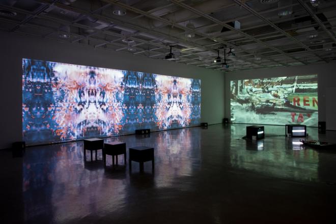 empty gallery space with video projections playing on gallery walls
