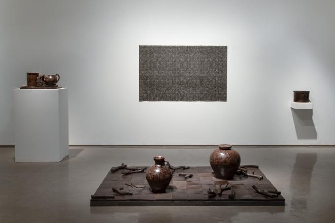 Collections of brown wood grain looking ceramic pottery staged on the floor and on tables with a large patterned wall piece in the background