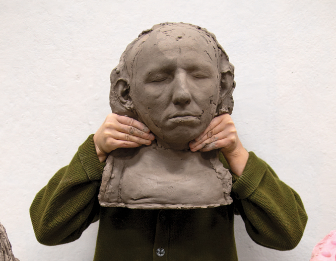 person holding a head bust sculpture in front of their face