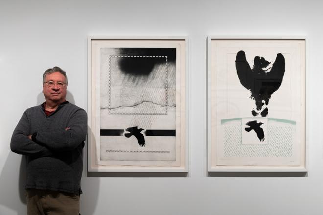 curator Joseph Scheer posing next to two prints on display