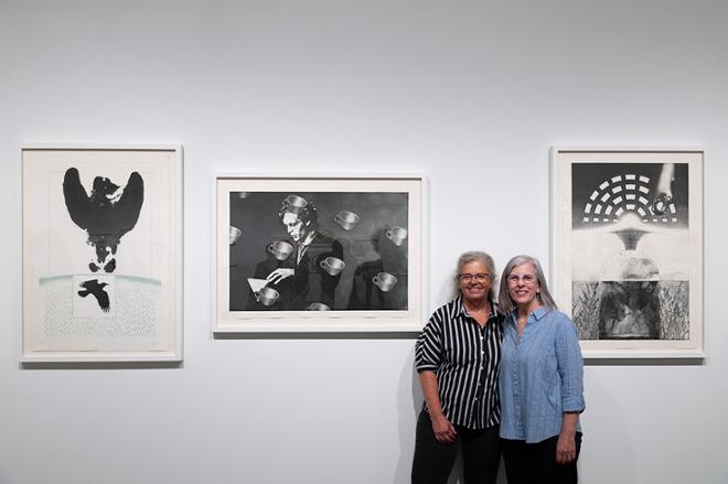 Sharon and Pam posing together in-between two prints on display