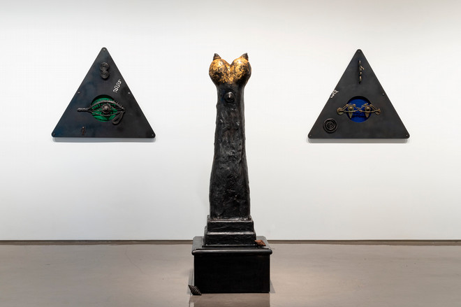 tower sculpture with two large triangle shaped pieces hung on each side on the wall