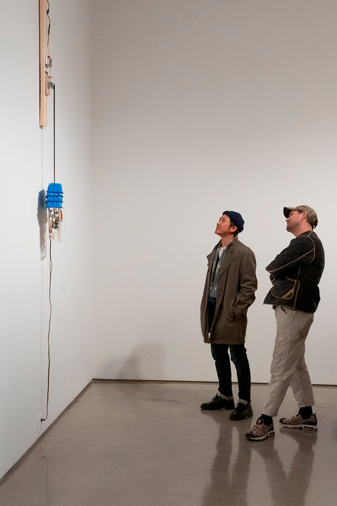 two people examining a tall sculpture hung on the wall