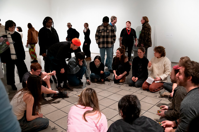 crowd forming a circle around a floor mat with small toy cars