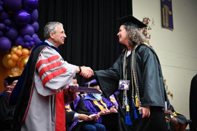 student wearing cap and gown shaking hands with the president