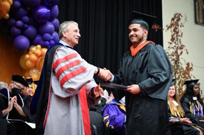student receiving diploma on stage shaking hands with the president
