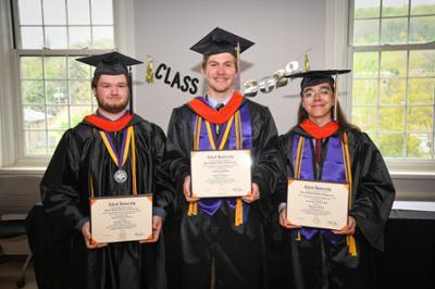 3 students with their diplomas smiling at the camera