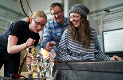 three students in glass art hot shop
