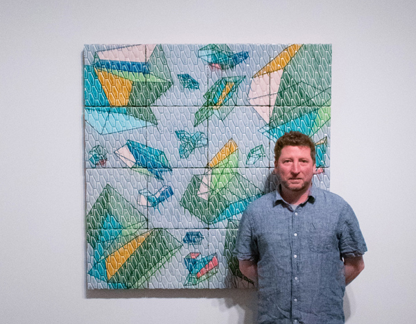 artist jason green posing alongside one of his works of art hung on the gallery wall
