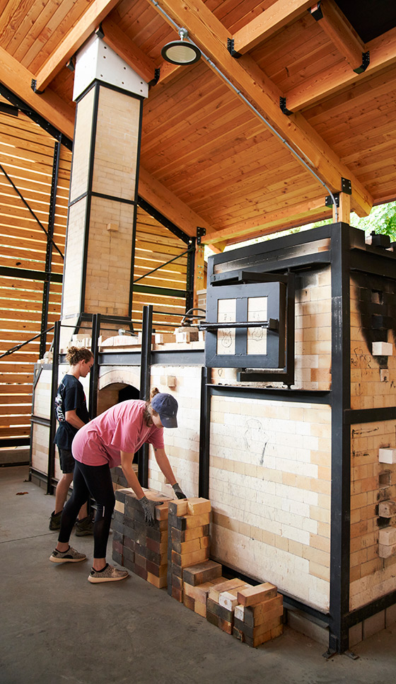 Students stacking bricks and preparing the large outdoor kiln structure at Alfred University’s kiln pavilion.