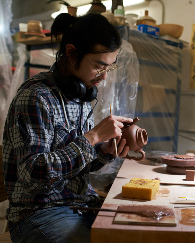 Student carefully detailing a clay teapot in the ceramics studio.