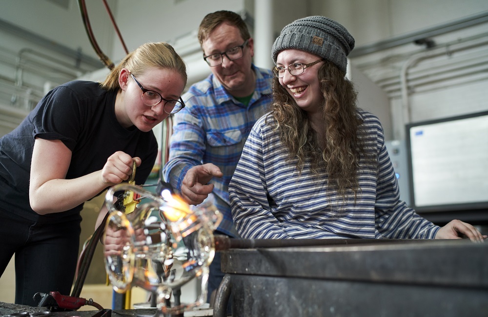 three students in glass art hot shop