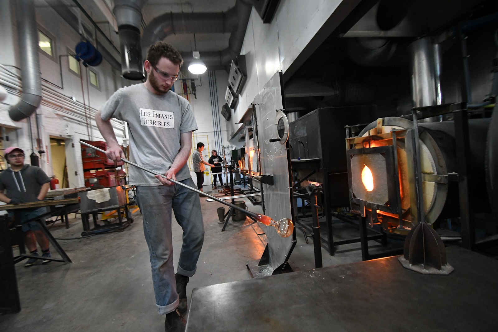 student walking to the glory hole with glass on a pole