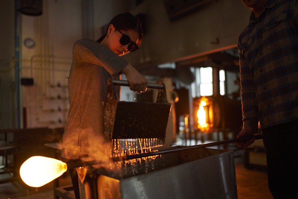 student blowing glass at the glory hole