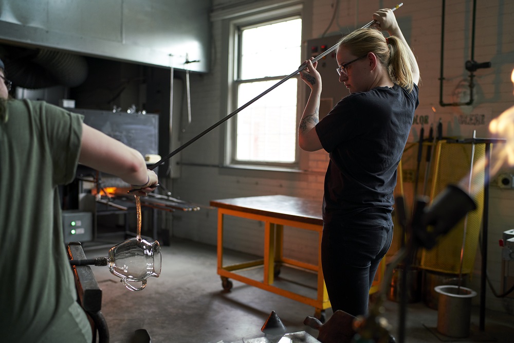 student putting glass in the glory hole