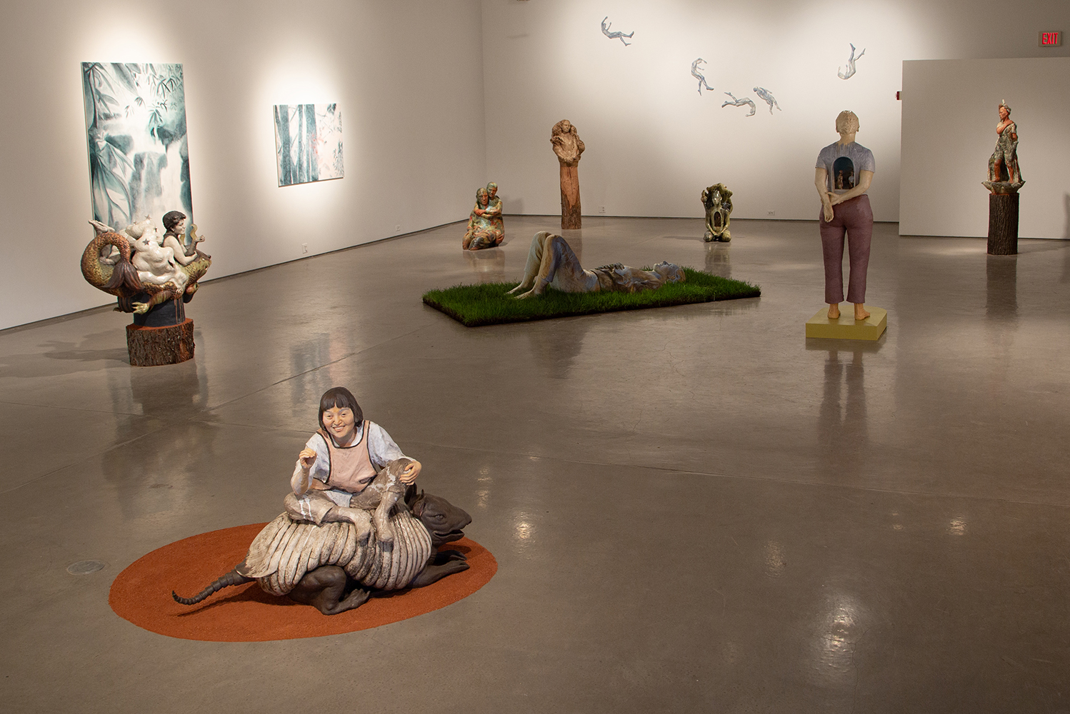 Art gallery with sculptures of human figures and abstract paintings on white walls and a polished concrete floor.