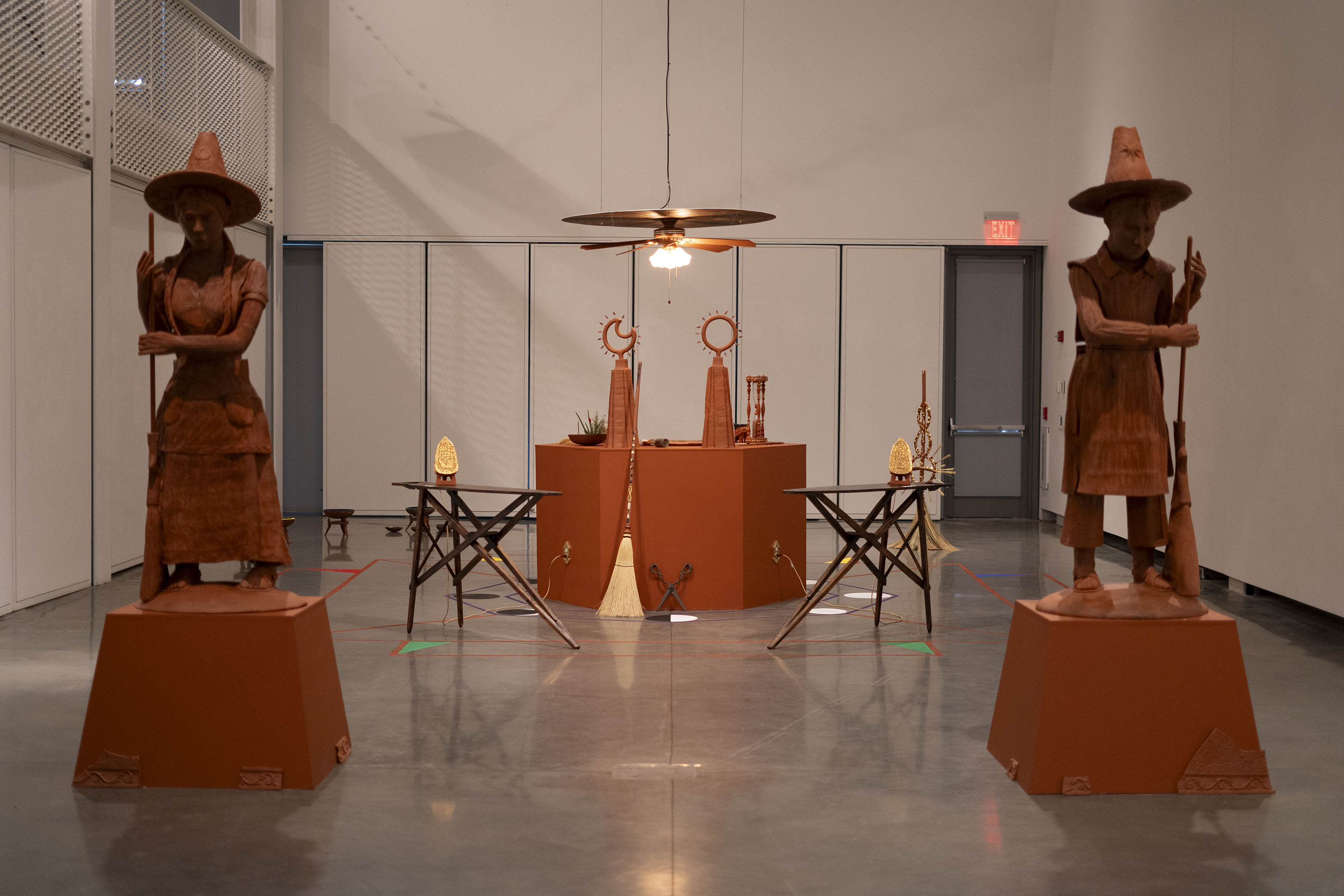 Exhibition space with statues and tables displaying artifacts under warm lighting.