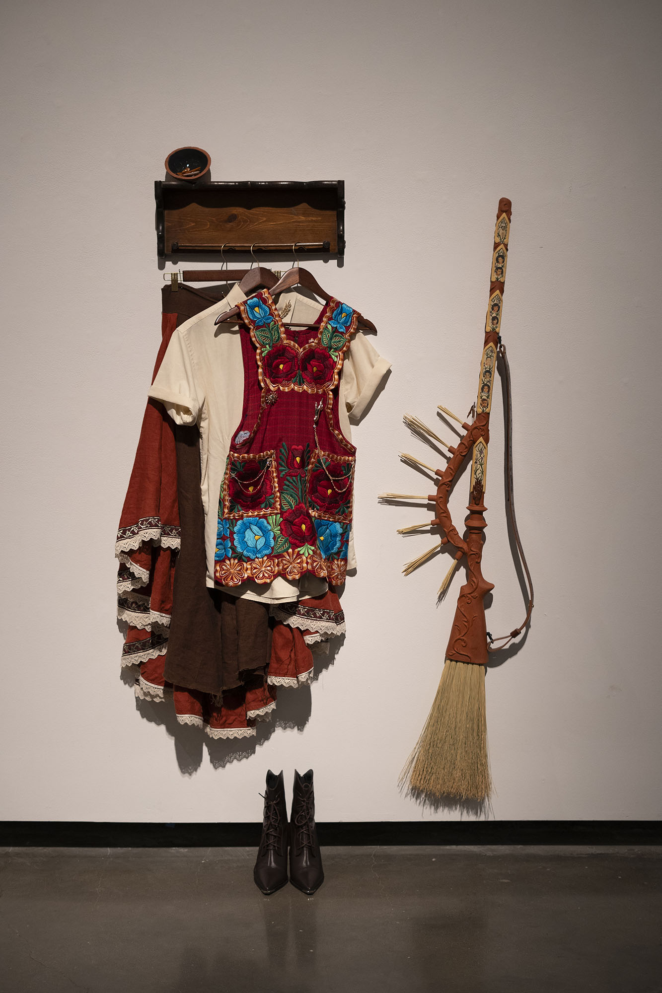 Clothing and a decorative broom hung on hooks against a plain wall.