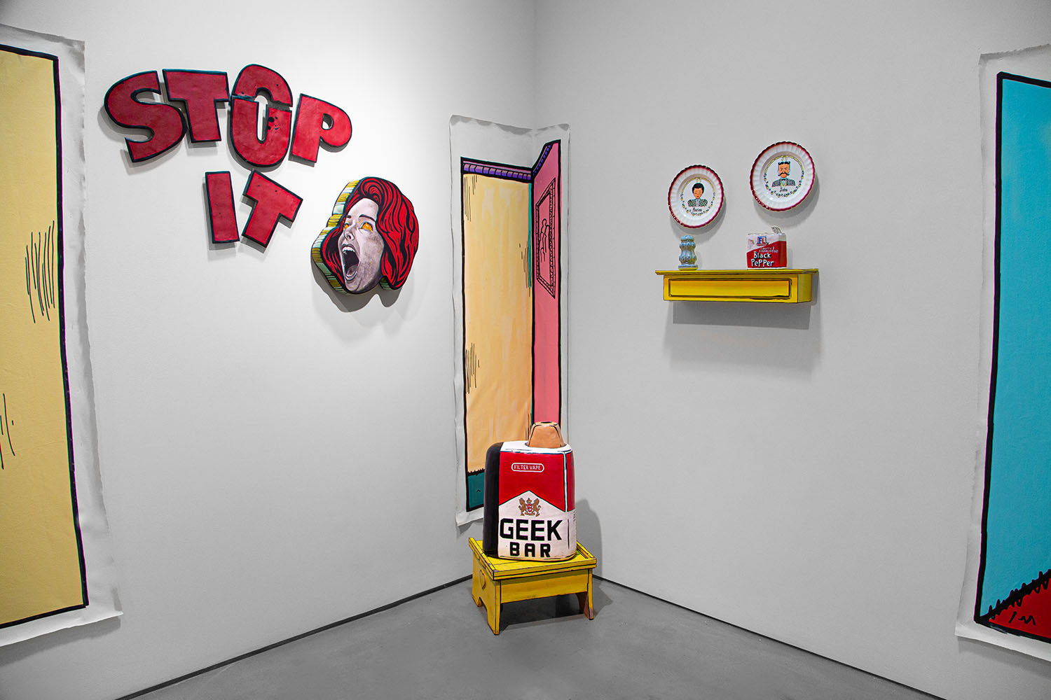 Art installation with 'STOP IT' text, screaming face, plates, and a box labeled 'GEEK BAR.'