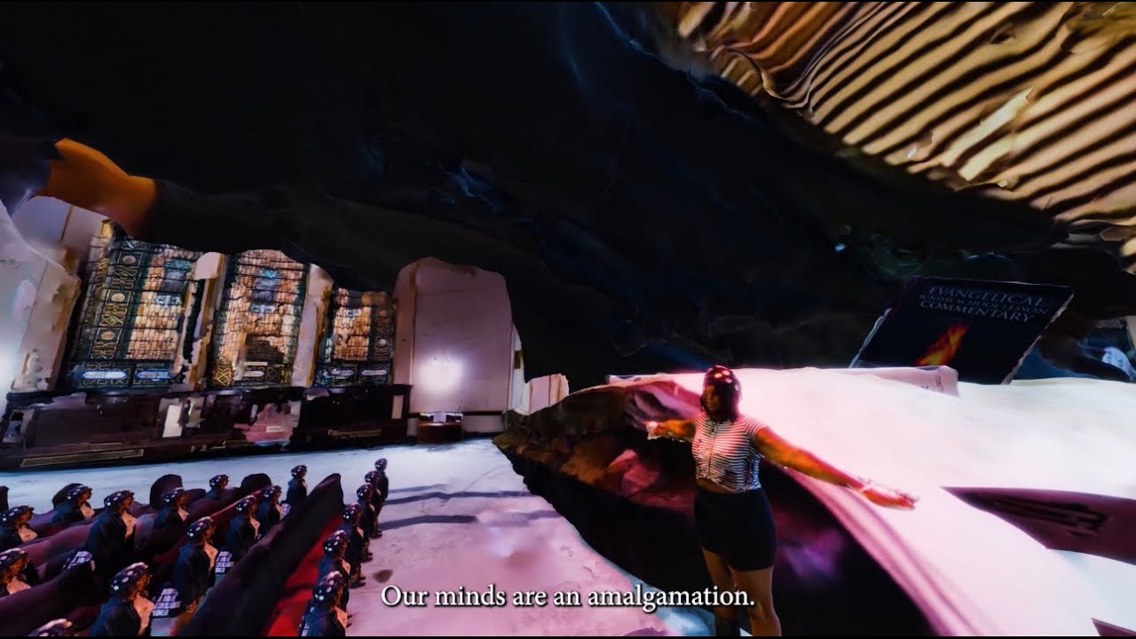 Person with arms outstretched in a surreal setting, audience visible, with the text 'Our minds are an amalgamation' at the bottom.